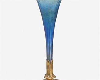 77
A Louis C. Tiffany Furnaces Gilt-Bronze And Art Glass Vase
Circa 1919-1928; New York, NY
Base signed: Louis C. Tiffany Furnaces, Inc. / Favrile / [L.C.T. monogram] / 158
The Louis C. Tiffany Furnaces gilt-bronze base with fluted foot and pentagonal floriform stem issuing a blue iridescent Favrile-style art glass trumpet vase with ribbed exterior
13.75" H x 5.625" Dia.
Estimate: $700 - $900