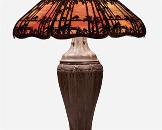 82
A Handel Teroca "Palm Tree And Sunset" Table Lamp
First-quarter 20th Century; Meriden, Connecticut
Signed: Handel / Pat'd. No. 979664
The "Teroca" shade with eight mottled pink slag glass panels encased in bronzed metal overlay with palm tree motif on a three-light baluster-form bronzed metal base with woven motif raised on four flared feet, electrified
Overall: 26.5" H x 20" Dia.
Estimate: $1,500 - $2,000