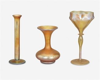 100
Three American Gold Art Glass Table Items
Late 19th/early 20th Century
First signed: L.C.T. / D 1087; Second signed: Aurene / 3058; Third signed: Quezal
Each gold iridescent art glass, comprising one L.C. Tiffany chalice with knopped stem, ribbed and pointed bowl, and blue-shaded interior, one Stueben Aurene bud vase with cylindrical body and flared rim, and one Quezal vase with bublous body, tall neck, and flared rim, 3 pieces
Largest: 8.625" H x 4.125" Dia.; Smallest: 6" H x 4.25" Dia.
Estimate: $800 - $1,200
