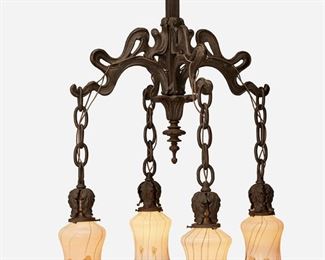 147
An Art Nouveau Patinated Bronze Chandelier
First-quarter 20th Century
Two shades numbered
The Art Nouveau four-light patinated bronze chandelier with stylized canopy and squared column with four free-form shaped arms, each issuing a drop pendant suspended from a chain link harness and terminating in a foliate-style socket and an iridescent white art glass shade with green leaf and vine motif, iridescent gold onion skin interior, and ruffled rim, electrified
30" H x 16" Dia.
Estimate: $1,000 - $1,500