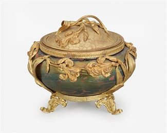 163
A Loetz-Style Gilt-Metal Mounted Art Glass Jar
Late 19th/early 20th Century
The iridescent purple and green oil spot glass jar mounted with gilt-metal floral overlay, floral motif lid, and raised on three scrolled feet
5" H x 6" Dia.
Estimate: $400 - $600