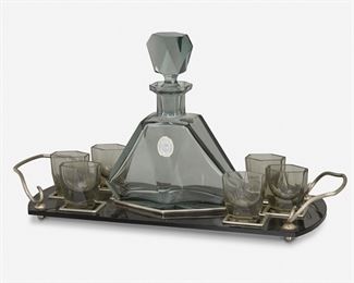 205
A Moser Cut Glass Apéritif Set
Second-quarter 20th Century; Karlovy Vary, Czech Republic (Bohemia)
Foil label: Bohemia Cristall / FH / XH
The Art Deco cut glass liqueur set in smoked glass, comprising a decanter with faceted stopper and six glasses atop a fitted black glass tray with silver-tone handles and fittings raised on four ball feet, 8 pieces
Overall: 9.5" H x 17.5" W x 6" D
Estimate: $400 - $600