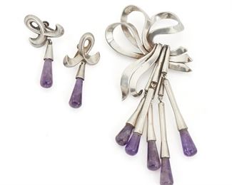 289
An Assembled Set Of Antonio Pineda Silver And Amethyst Jewelry
1953-1979; Taxco, Mexico
Crown mark for Antonio Pineda; Further stamped: Eagle 17 / Hecho en Mexico / Silver / 970 / PR527
Comprising a bow brooch suspending trumpet style silver drops tipped with amethyst (4.5" H x 2.25" W) and a pair of screw-back earrings (2" H x 1" W) designed with a ribbon motif with amethyst drops, 3 pieces
71.5 grams
Estimate: $400 - $600
