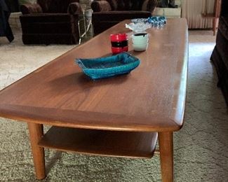 BID ITEM: Danish Modern Teak "Surfboard style" coffee table damage to lower tier shelf where it connects to leg (does not affect functionality)  Measures 69" Long, 23" at greatest width and 16" Height 