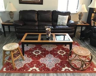 Dark brown faux leather manual reclining sofa, matching coffee and end tables, pair of lamps, area rug, step stool and rattan foot stool.