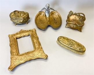 191	Group of Art Nouveau Gilt Bronze Items	Art Nouveau NB Rogers SP Jewelry Casket. Produced NB Rogers SP Co. (Nathaniel Burton Rogers b. 1848, member of the Rogers Silversmith dynasty). Features a cherub figure and is marked 943. 5 1/2"L x 3.5" W 4.5" H. Gilt brass shoe brush. Features a Gorgon-like face with floral design. Some gilding is damaged exposing metal underneath. 8" L x 3" W x 3"H. Art Nouveau Jewelry Casket. Features curving sides and handle with clover designs throughout. Pin clasp on left side is damaged and not attached. Marked underneath "TRADEMARK J.B. SIGNIFIES THE BEST 645". 5" L x 4" W x 4.5" H. Gilt and Painted Bronze Jewelry Tray. Consists of two pieces, a nude female figure painted silver supporting a segmented gilt tray with two recesses for jewelry. Figure is attached with a single flat screw. 8" L x 8" W x 5.5" H. Gilt bronze picture frame featuring interlocking curving design with a crown and heart design at the top. Has wear consistent with age. The back of
