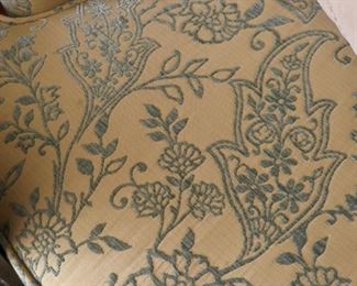 Close view of upholstery of two wing back chairs and two footstools. Blue embroidery on cream color ground.