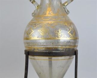 23 Glass Amphora in Wrought Iron Stand Large amphora form glass vase, with hand painted gilt decoration, in wrought iron stand. 24 3/4"H (vase 21 1/2"H). Losses to gilt decoration, paint on stand.