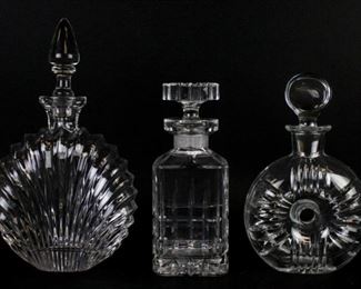 87 3 Crystal Decanters Unsigned square decanter, 9"H including stopper; unsigned shell form decanter, 11 1/2"H including stopper; signed Atlantis circular decanter, 8 3/4"H including stopper. Stopper loose on shell decanter