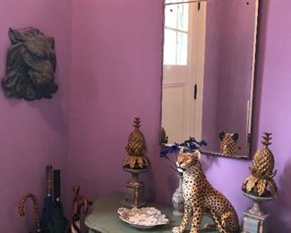 Console table, ceramic cheetah, metal pineapple decor, copper lion head, and umbrellas with canister