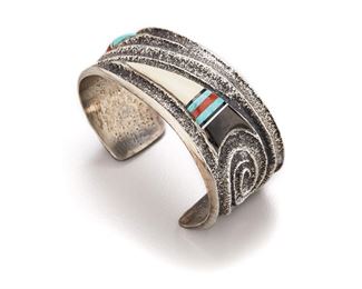 198
A Preston Monongye Sandcast Cuff
1927-1987, Hopi
Marked with artist's symbol to interior
A tuffa cast silver cuff bracelet with swirls to ends and inlaid with bone, turquoise, onyx, and coral points
6" L x 1.10" H <br /> 6 H
75.8 grams
Estimate: $3,000 - $5,000