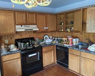 Household goods in kitchen including old tins, bottles and jars, china pieces, and come ceramic collectible statues.