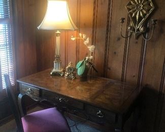 Desk with burled wood top, brass lamp, candle holder wall unit, and side chair