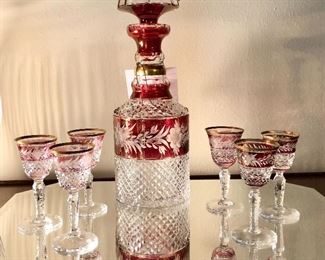 Antique cranberry cased glass decanter with six cordials. Diamond cut, etched floral design.