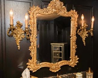 A Pair of Louis XV Style Gilt Metal Sconces and Gilt Wood Mirror. 
Dimensions: Sconces Height 12 x width 8 ½ inches. Mirror Height 37 x width 23 ½ x depth 1 1/5 inches.
Sconces $1,000.00 Mirror $600.00