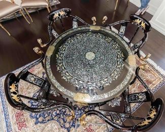 An Important Lacquered and Mother of Pearl Inlaid Table and Chairs. Edition of 250. Signed Illegibly and Numbered 240/250. 

The laquered and inlaid table and chairs purportedly formerly of the Onassis estate having Persian accents, the table of circular form having intricately inlaid abalone scroll decoration with animalier form accents to center, the edge bordered with inlaid floral, foliate and animalier decoration with four brass plates, the skirt with brass etched plates, raised on lacquered legs. The chairs with concave crest rail with inlaid Shirdal or Persian winged lions, the sinuous arms with abalone inlay  and ending in brass ram’s head supported by two backsplats with inlay over the shaped seats, raised on stylized cabiriole legs joined by X stretchers and ending in animal paw feet.
Dimensions: Table Height 30 x diameter 40 ½ inches. Chairs: Height 35 ½ x width 35 x depth 21 ¼ inches.   For the table and chairs $150,000.00

