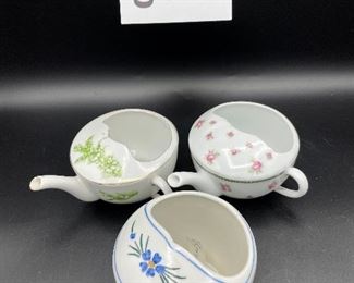 Lot 8255. $70.00. Lot of 7 side- handled infant/hospital/invalid feeders. All have a design and/or are colored in some way. 1) signed Vienna, Austria Edelweiss floral design,"Fur Genesung", which translates to "for recovery", 2) Cobalt blue color with floral images, 3) Purple violets, Vienna, Austria, 4) Pink rosebud design made in Victoria, Austria, 5) White with blue flower from London Covent Garden, 6) Lily of the Vally, marked #357, and 7) blue floral design embellishes the entire feeder cup.
