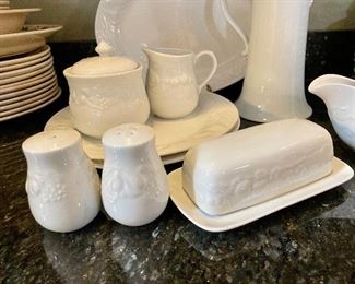 Lot 8295. $75.00. 10 pc. of White Fruits de blanc dinnerware serving pieces, featuring fruit decor in relief on all pieces, includes: 14" oval platter, covered butter dish, creamer, sugar, salt and pepper, gravy/saucer, 2 dinner plates or cookie plates, and a white Kaiser tankard or pitcher 9.5" T.