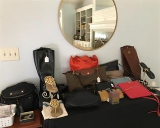 Family Room:  Bagged costume jewelry is to the left of numerous designer items including:  two pairs of TORY BURCH boots and two pairs of TORY BURCH sandals (sizes 7 and 7-l/2); MADEWELL, LONGCHAMP and MARC JACOBS totes; a MICHAEL KORS cross body; a small KATE SPADE straw clutch; and numerous GIGI cross body purses.  A TUMI carry-on bag is nearby.  (The round wall mirror is for sale, too!)