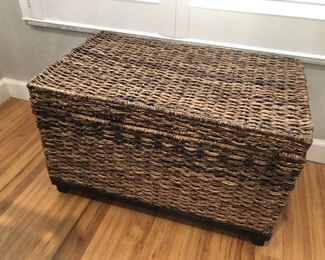 One of two woven lift top storage trunks