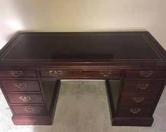 Sligh wood desk with gold details and handles. It has seven drawers and measures 26” x 56” x 30”.
