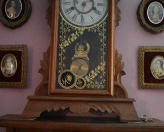 Antique Gingerbread Mantle Clock in Beautiful Condition featuring Carved Wood, Porcelain Face, Pendulum with unusual Compass styling, and Gold Leaf Trim Painting on Glass sitting atop Wall Shelf with Porcelain knob and surrounded by Collectible Victorian Ladies in Curved Glass Oval Frames
