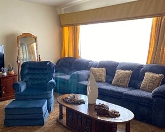 Lovely living room items includes dark blue suede loveseat with matching ottoman, large three cushioned  sofa with decorative accent pillows, and a matching two cushioned sofa to complete the set. Wooden coffee table with decorative items atop it.
