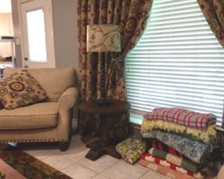 Upholstered chair with brass button trim, side table and lamp, assortment of throws