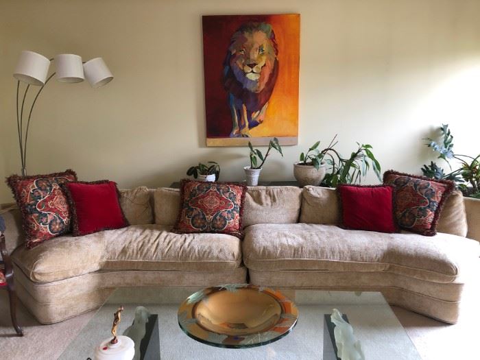 2 Piece (L&R) Angled Cream Textured Sofa With 2 Matching Ottomans.  The Ottomans Can Be Sold Separately.  Sofa Table Behind And Plants.  Large "Lion" Painting With Great "Sunset" Colors