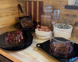 Copper cookies cutters, kitchen utensils, wooden cutting board, black depression glass plates, serving platters and footed bowl
