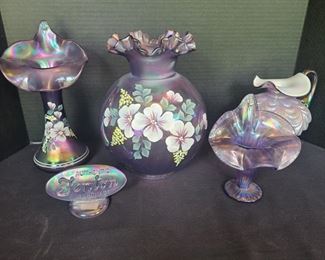 Five stunning purple Fenton glass pieces. Two hand painted vases, a pitcher, a hand painted lamp cover and small creators mark. Lamp cover measures 8" x 10". Largest vase measures 6" x 11". https://ctbids.com/#!/description/share/974506