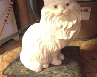 A ceramic kitty content on a padded stool. 