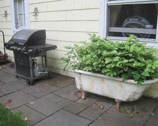 Gas grill and claw foot bathtub with or without plants.
