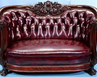 063a - Rounded mahogany heavily carved parlor sofa by Karpen, has dragon carved in back and dolphin arms, leather with tufted back, 36 in. T, 61 in. L, 25 in. D.