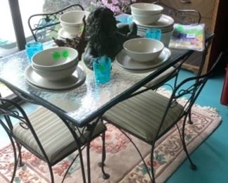 The patio table with the glass top  and 4 metal chairs.  Pink dogwood plant in corner.