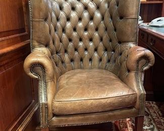 Tufted leather-upholstered wingback chair with nailhead trim. On casters. 