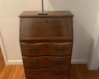 Wooden vintage secretary with small accent lamp.