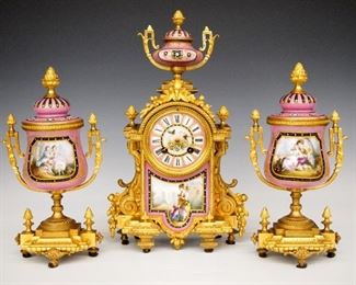 Japy Freres French Clock Set - A turn of the century French three piece clock set by Japy Freres.  8-day time and strike movement with porcelain dial, Roman numerals and fancy gilded hands.  Gilded Bronze case with hand painted porcelain insert and urn finial with two urn form porcelain garnitures with hand painted court scenes and gilded Bronze mounts.  Some minor wear, running when cataloged.  14" high overall.  ESTIMATE $600-800

