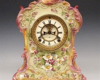 Ansonia La Floride China Shelf Clock - A turn of the century Ansonia "La Floride" model china shelf clock.  8-day time and strike movement with visible escapement, two part porcelain dial and Roman numerals.  Royal Bonn porcelain case with floral decoration and gilded detail.  Some wear, crazing, hairline and small repair in dial, running when cataloged.  14 1/4" high.  ESTIMATE $200-300

