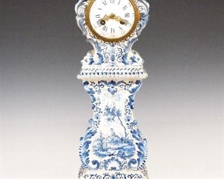 Delft Miniature Tall Clock - A 19th century Dutch Delft miniature tall clock.  8-day time and strike movement by Vincenti et Cie, Paris with a porcelain dial, Roman hour numerals and Arabic minute numerals and fancy Gilded filigree hands.  Delft Rococo style earthenware case with Lion masks and foliate scrolls, hand painted Blue decoration with rural scenery and floral detail.  Several old repairs to the upper case with some filling and re-glazing, running when cataloged.  19 3/4" high.  ESTIMATE $1,000-1,500

