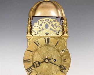 W & H Lantern Clock - An early 20th century Winterhalder & Hofmeier Lantern clock.  High quality 8-day time & strike movement with quarter hour striking on two cast bells, Brass with  Silvered chapter ring, Roman numerals and cast spandrels.  Brass case with upper bell support, cast reticulated crests, turned columns and feet, cast Sun masks on side access doors.  Minor wear, running when cataloged.  Plaque at front states "Presented to, Richard Clowes, by A J Worthington & Co., Portland Mills, Leek, as a mark of esteem on the, completion of Fifty Years, service with the firm, May 28th, 1895".  Minor wear, tarnish on chapter ring, running when cataloged.  15 3/4" high.  ESTIMATE $1,000-1,500
