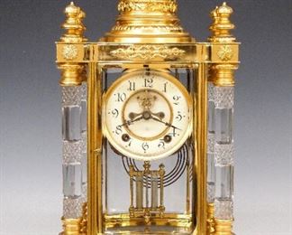 Ansonia Utopia Crystal Regulator - A turn of the century Ansonia "Utopia" model Crystal Regulator.  8-day time and strike movement with visible escapement, two part porcelain dial and Arabic numerals.  Polished Brass case with pressed glass columns and gilded detail.  Case restored, running when cataloged.  17" high.  ESTIMATE $600-800
