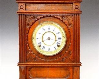 Waterbury Cabinet F Shelf Clock - A late 19th century Waterbury "Cabinet F" model Victorian shelf clock.  8-day time and strike movement, a two-part porcelain dial with Roman numerals and embossed Brass bezel.  Carved Eastlake style Walnut case with gallery top, circular Brass door with beveled glass, flanked by flat fluted columns above an oval frieze and molded base.  Paper label on back 50% intact.  Older finish with some wear, shrinkage cracks, hairline in dial, running when cataloged.  19 1/2" high. 
