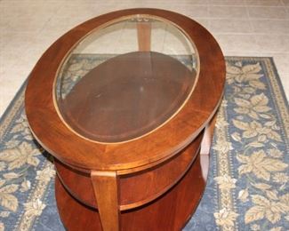 Oval wood and glass coffee table with shelves.