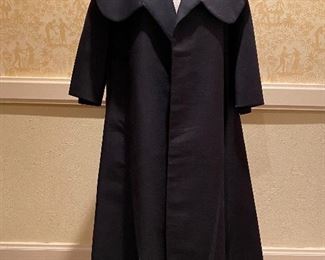 A vintage Neiman Marcus black cape style coat with a draw string belt that is on the exterior on the backside yet is pulled and tied in the interior.   