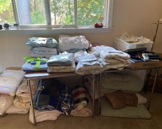 bedroom main floor room has many linens and bedspreads, mattress covers, pillows, sheets.