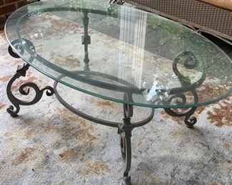 Oval indoor/outdoor cocktail table with wrought iron base and tempered glass top.