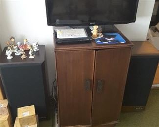 Samsung TV. Vintage Infinity Wood Speakers either side, Model SM-155, Small 2 Door Audio Cabinet, Small DVD Player on top of cabinet. Best Friends Statue and Kittie Cat Blue Mouse Pad.