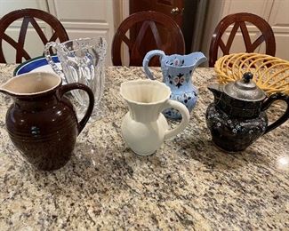 Le Creuset pitcher $35, whiter ceramic $5, Alexandria Pottery tea server with copper bottom $$75, yellow ceramic bread basket $20, blue floral pitcher $50, and glass tall butterfly pitcher $40