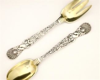 Lot 14: Two Tiffany & Co. "Dolphin" pattern Sterling Silver serving utensils.  Includes a serving fork and spoon with Gold washed bowls and marine themed handles.  Each marked "Tiffany & Co., Sterling, 1883 M".  11.89 troy ozs total weight.  Slight wear to surface and gold wash, monogrammed at back of bowls.  Each 10 1/4" long.  ESTIMATE $600-800